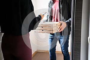 Pizza delivery phone app concept. Food deliverer at home door and customer using cellphone to pay, tip or give online rating.