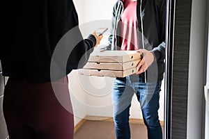 Pizza delivery phone app concept. Food deliverer at home door and customer using cellphone to pay, tip or give online rating. photo