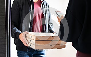 Pizza delivery to home door after online order with mobile phone. Deliverer holding fast food boxes and customer using smartphone. photo