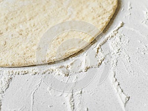 Pizza dough in flour. Ingredient for making homemade pizza on a white table. Close-up