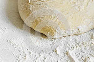 Pizza dough in flour. Ingredient for making homemade pizza on a white table. Close-up