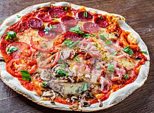 Pizza `Four Seasons` with Mozzarella cheese, ham, tomato sauce, salami, bacon, mushroom, pepper, Spices and Fresh basil. Italian p