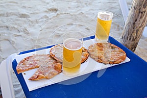 Pizza and glasses of beer on a tray on a chaise lounge.
