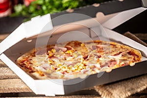 Pizza with ham, corn and cheese in a half-open white pizza box