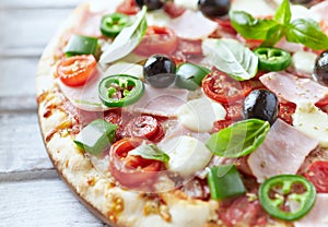 Pizza with ham, mozzarella cheese, cherry tomatoes, green and jalapeno pepper, black olives and fresh basil.