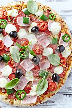 Pizza with ham, mozzarella cheese, cherry tomatoes, green and jalapeno pepper, black olives and fresh basil.