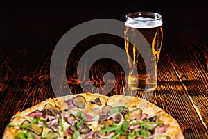 Pizza with ham on wooden table near a glass of beer