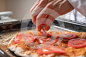 The pizza maker puts tomato slices on the pizza