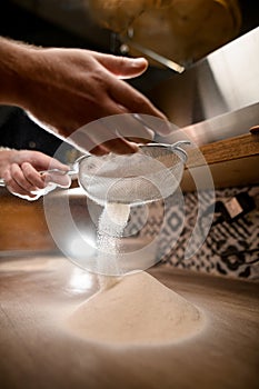 Pizza maker& x27;s hands sift white flour through a sieve on a wooden table