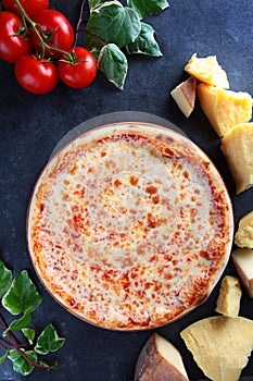 Pizza Margarita. Hard cheese in chunks on a dark background. View from above. Vertical photo.