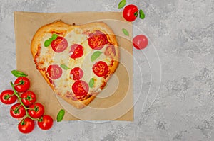 Pizza Margherita shaped heart with cherry tomatoes, mozzarella and basil on a gray concrete background.