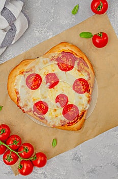 Pizza Margherita shaped heart with cherry tomatoes, mozzarella and basil on a gray concrete background.