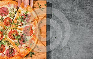 Pizza with mazzarella cheese, pepperoni and tomatoes on gray background, girl`s hand takes slice of pizza. Pizzeria advertising