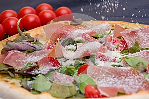 Pizza with meat and herbs, sprinkled with cheese, cherry tomatoes