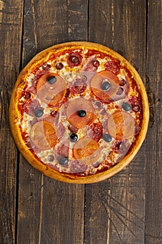 Pizza with meat, tomatoes, ham and olives. On a wooden table