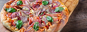 Pizza with Mozzarella cheese, ham, tomato sauce, salami, onion, pepper, Spices and Fresh basil. Italian pizza on wooden table