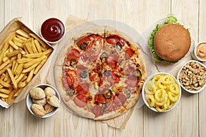 Pizza, onion rings and other fast food on wooden table, flat lay