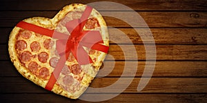 Pizza pepperoni shaped heart with red ribbon bow for Valentine`s Day on rustic dark black background. Top View. Holiday