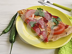 Pizza piece portion sausage fork pepper knife towel tomato on white wooden