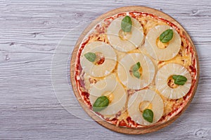 Pizza with pineapple rings and basil on the table