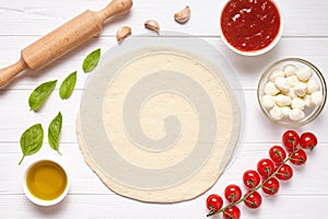 Pizza preparation. Baking ingredients on the kitchen table: rolled dough, mozzarella, tomatoes sauce, basil, olive oil