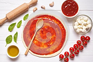 Pizza preparation. Baking ingredients on the kitchen table: rolled dough with tomatoes sauce