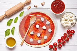 Pizza preparation. Ingredients on the kitchen table: rolled dough with tomatoes sauce, basil, olive oil, mozzarella