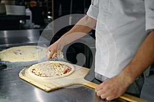 Pizza preparation process with closeup chef hands sprinkling cheese