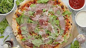 Pizza with prosciutto and arugula. Served with fresh ingredients on sides