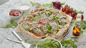 Pizza with prosciutto and arugula. Served with fresh ingredients on sides