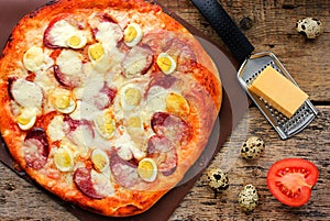 Pizza with quail eggs, sausage, cheese and tomatoes on a wooden