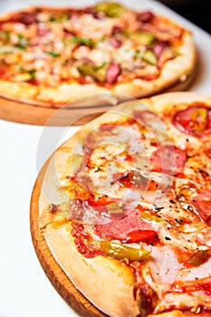 Pizza with salami, bell pepper, tomatoes and cheese, pickles, bacon and sausages on a light background. Close-up, selective focus