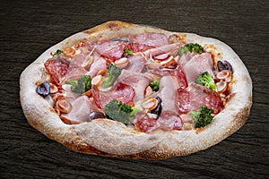 Pizza with salami, ham, vienna sausages, kalamata, olives, broccoli, pelati, pesto. Neapolitan round pizza on wood background