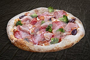 Pizza with salami, ham, vienna sausages, kalamata, olives, broccoli, pelati, pesto. Neapolitan round pizza on wood background