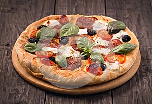 Pizza with salami, mozzarella, olives and basil on rustic wooden