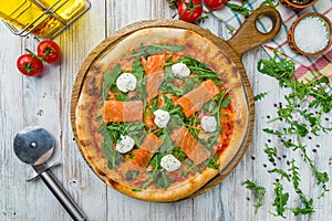 Pizza with salmon and Philadelphia cheese and aragula on white wooden table