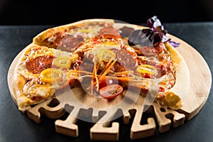 Pizza with sausage and tomatoes on a wooden round tray with a carved inscription `Pizza`.