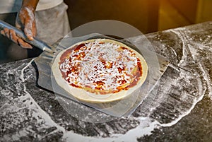 Pizza on shovel in hands of the chef in kitchen