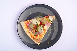 Pizza slice with pepperoni, salami, melted mozzarella cheese, pickles and dill in black plate on white background