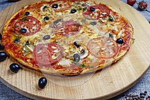 Pizza with slices of sausage, cheese, olives and tomatoes cut into rings. Pizza on a light wooden platter.