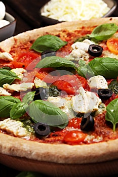 Pizza with tomatoes, mozzarella cheese, black olives and basil. Delicious italian pizza on wooden pizza board