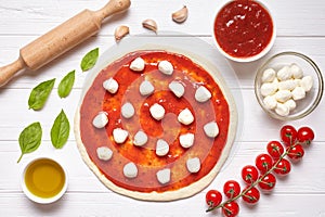 Pizza traditional preparation. Ingredients on the kitchen table: rolled dough with tomatoes sauce