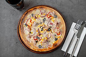 Pizza with tuna, onions and olives on cutting board on stone table