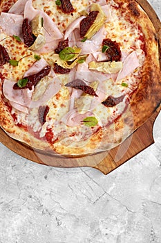 pizza with veal, ham, cheese and sun-dried tomatoes on a gray table