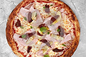 pizza with veal, ham, cheese and sun-dried tomatoes on a gray table