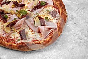 pizza with veal, ham, cheese and sun-dried tomatoes on a gray table