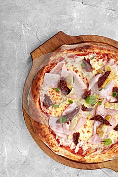 pizza with veal, ham, cheese and sun-dried tomatoes on a gray table