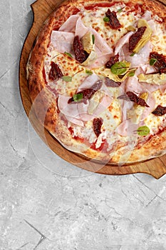 pizza with veal, ham, cheese and sun-dried tomatoes on a gray table