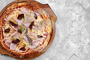 pizza with veal, ham, cheese and sun-dried tomatoes on a gray table
