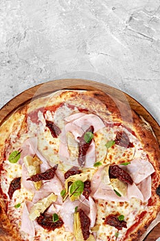 pizza with veal, ham, cheese and sun-dried tomatoes on a gray table